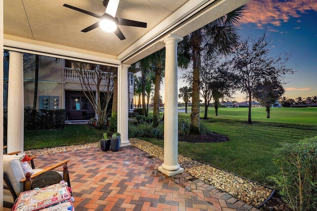 patio terrace at dusk featuring a lawn and ceiling fan