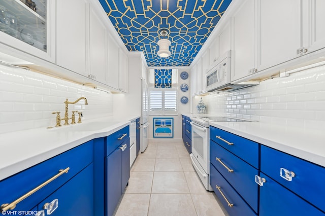 kitchen featuring white appliances, sink, light tile patterned floors, blue cabinetry, and white cabinetry