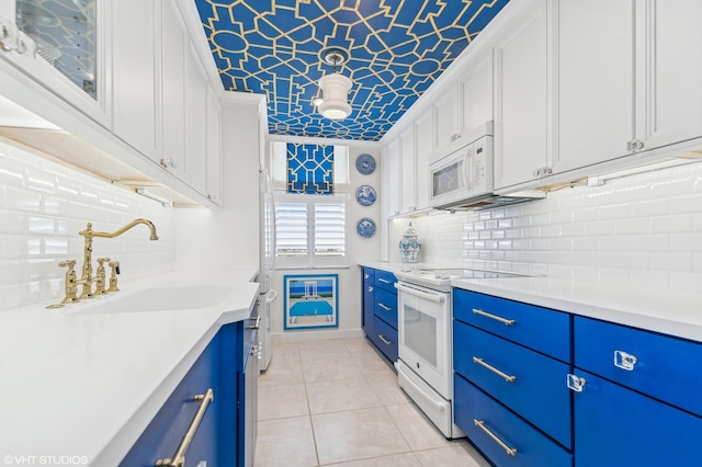 kitchen with sink, light tile patterned floors, blue cabinets, white appliances, and white cabinets