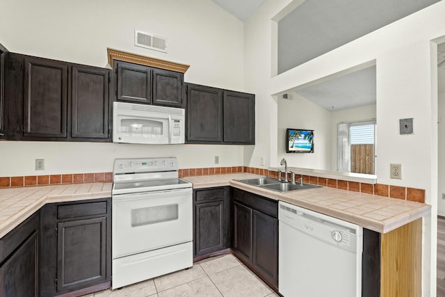 kitchen with sink, kitchen peninsula, lofted ceiling, white appliances, and light tile patterned flooring