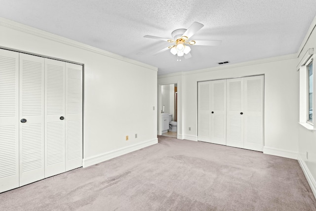 unfurnished bedroom featuring ensuite bathroom, a textured ceiling, light colored carpet, ceiling fan, and crown molding