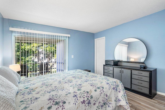 bedroom with access to exterior, a textured ceiling, and light hardwood / wood-style flooring