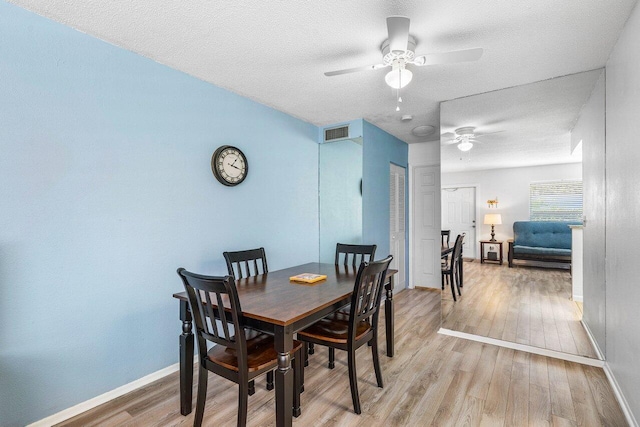 dining space with a textured ceiling, light wood-type flooring, and ceiling fan