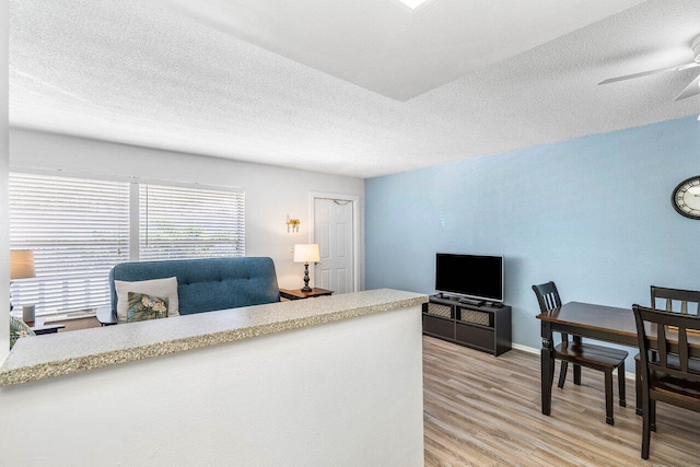 living room with ceiling fan, a textured ceiling, and light wood-type flooring