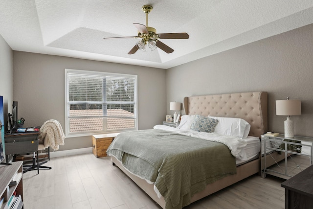 bedroom featuring ceiling fan, light hardwood / wood-style flooring, and a tray ceiling