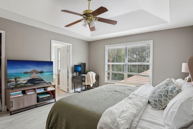 bedroom featuring ceiling fan, light hardwood / wood-style flooring, a raised ceiling, and a textured ceiling