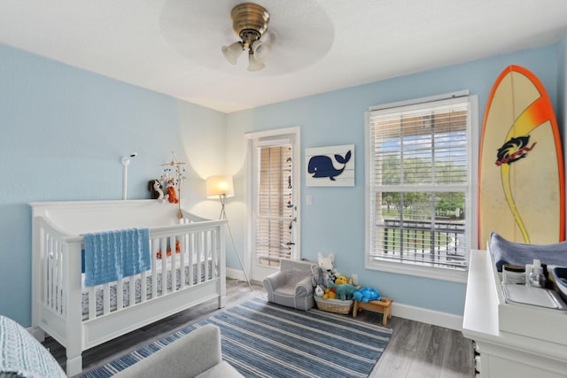 bedroom with ceiling fan, a crib, and wood-type flooring