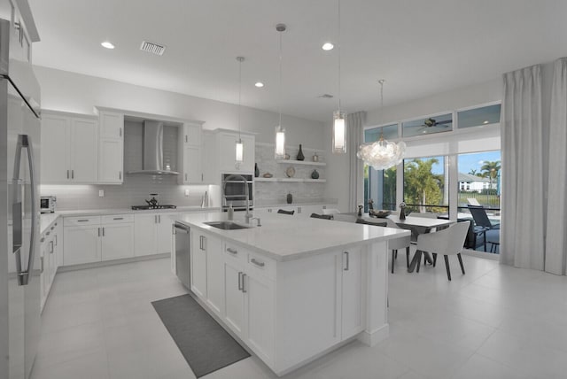 kitchen featuring sink, an island with sink, wall chimney range hood, and white cabinetry