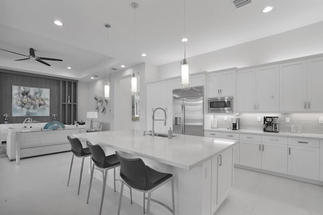 kitchen with built in appliances, decorative light fixtures, a center island with sink, white cabinets, and sink