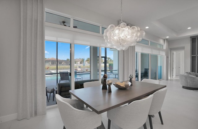 dining area with a raised ceiling, a notable chandelier, and a water view