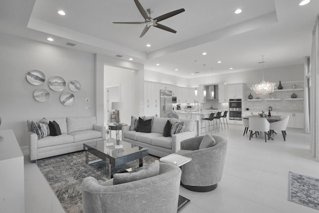 living room featuring ceiling fan, a tray ceiling, light tile patterned floors, and sink