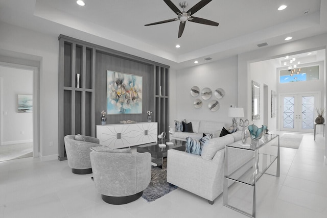 tiled living room with ceiling fan with notable chandelier, french doors, and a tray ceiling