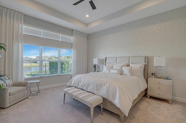 bedroom with light colored carpet, ceiling fan, and a tray ceiling