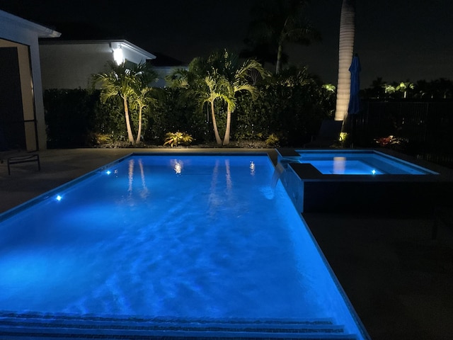 pool at twilight featuring an in ground hot tub