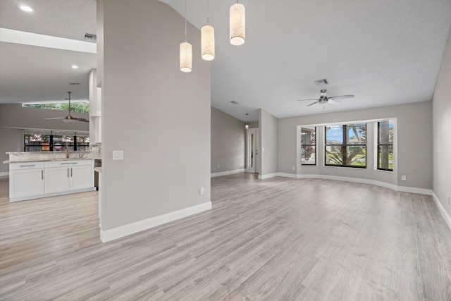 unfurnished living room with lofted ceiling, sink, ceiling fan, a textured ceiling, and light hardwood / wood-style floors