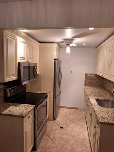 kitchen with light stone countertops, stainless steel appliances, white cabinets, and sink