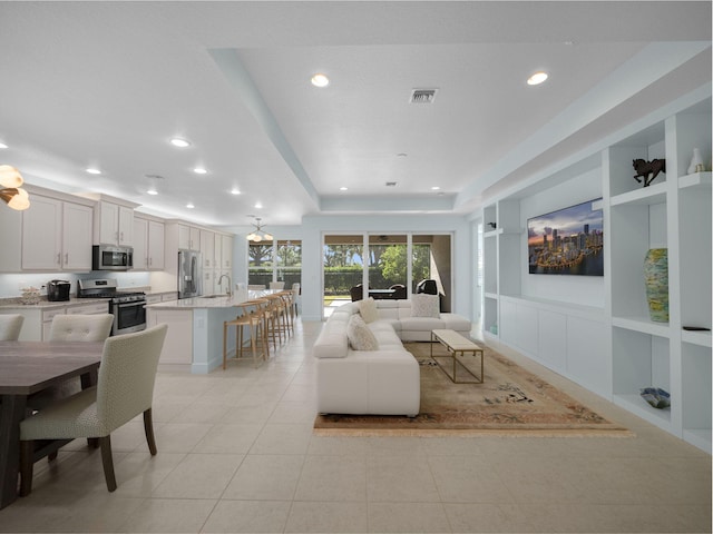 living room featuring sink, built in shelves, light tile patterned floors, and a raised ceiling