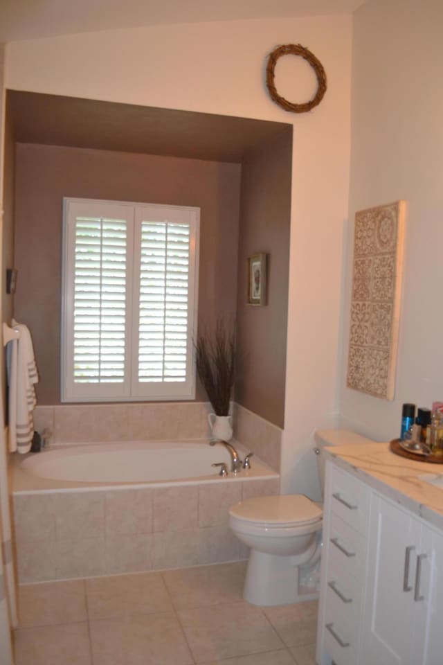 bathroom with tiled bath, toilet, vanity, and tile patterned flooring