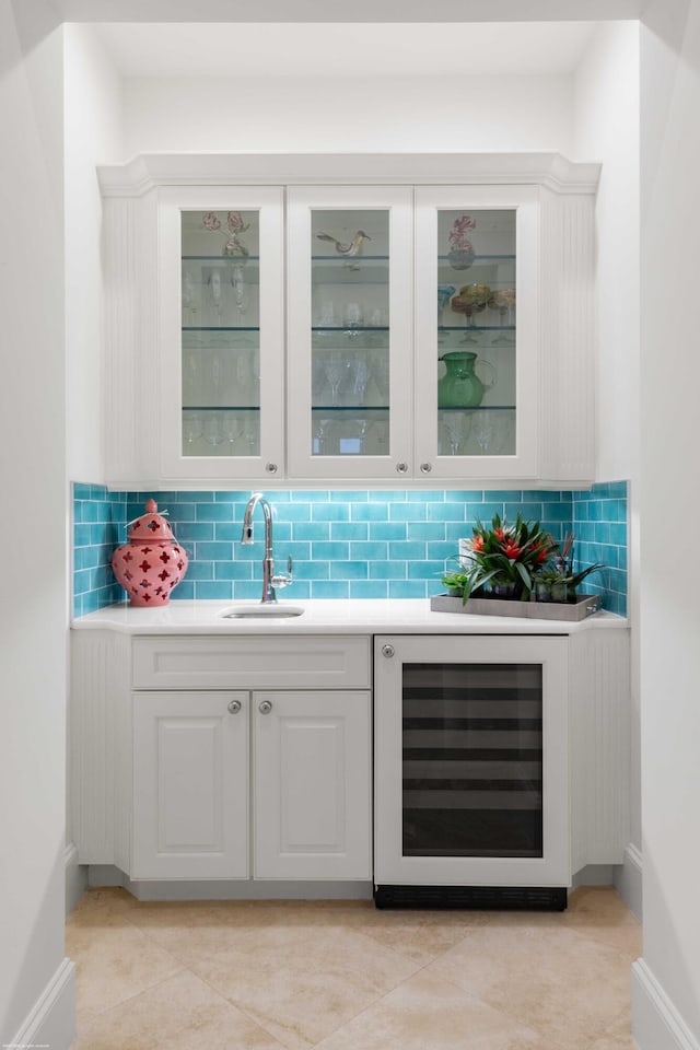 bar featuring decorative backsplash, beverage cooler, sink, white cabinets, and light tile patterned flooring