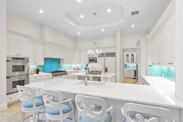 kitchen featuring white cabinets, a raised ceiling, sink, hanging light fixtures, and built in appliances