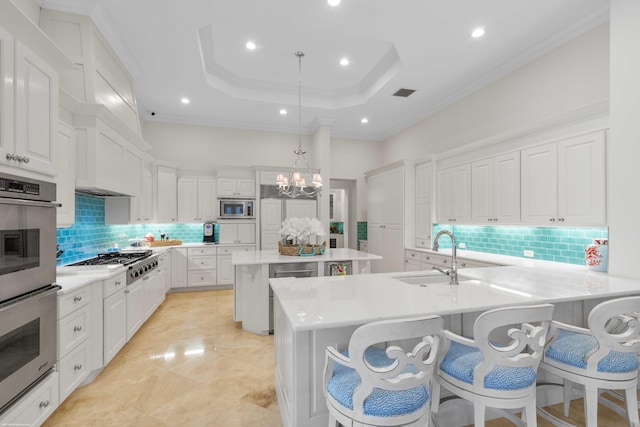 kitchen with a kitchen bar, stainless steel appliances, a tray ceiling, sink, and decorative light fixtures