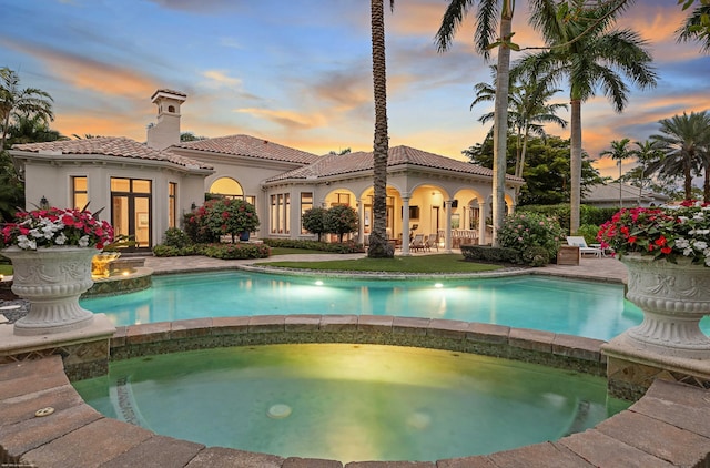 pool at dusk featuring an in ground hot tub and a patio