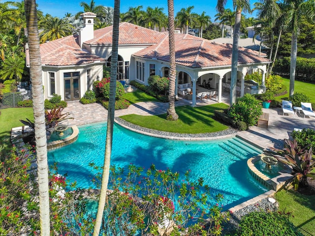 rear view of property with a lawn, a patio area, a swimming pool with hot tub, and french doors