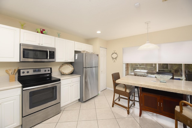 kitchen with light tile patterned flooring, appliances with stainless steel finishes, white cabinetry, and hanging light fixtures