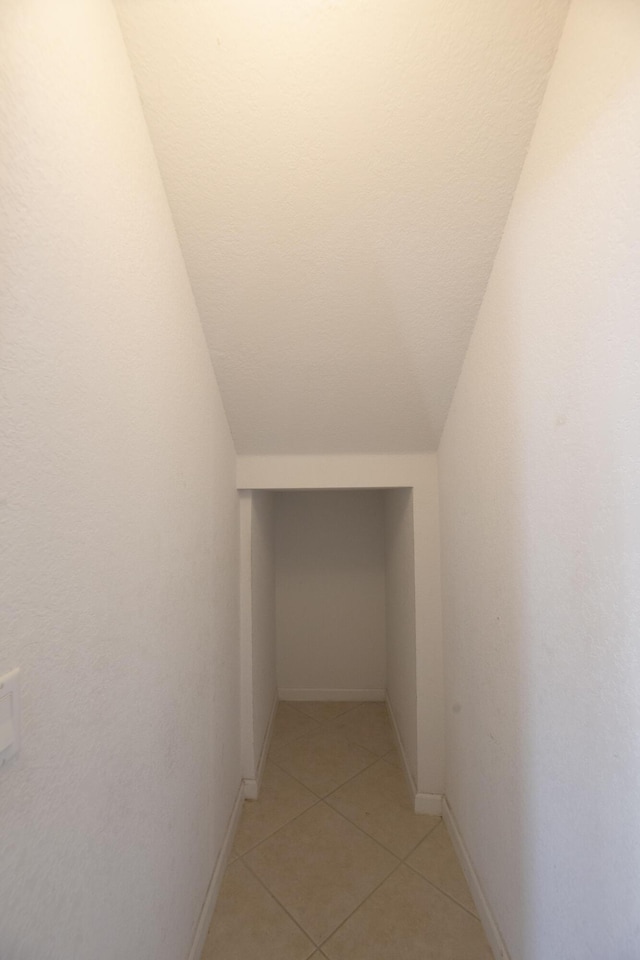 corridor featuring lofted ceiling and light tile patterned flooring