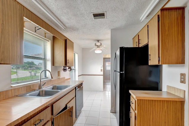 kitchen with light tile patterned floors, black refrigerator, dishwasher, a textured ceiling, and sink