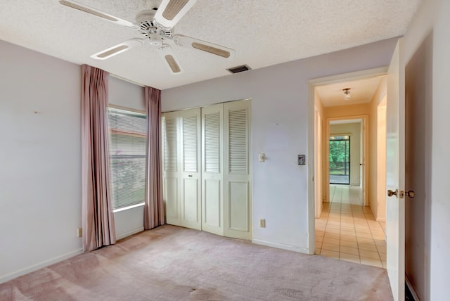 unfurnished bedroom with a textured ceiling, ceiling fan, a closet, and light colored carpet