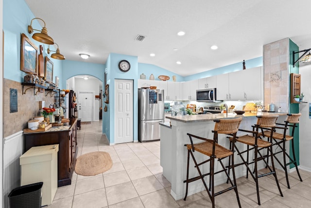 kitchen with kitchen peninsula, a breakfast bar area, stainless steel appliances, lofted ceiling, and white cabinets