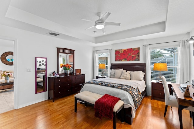 bedroom with a raised ceiling, ceiling fan, and light hardwood / wood-style floors