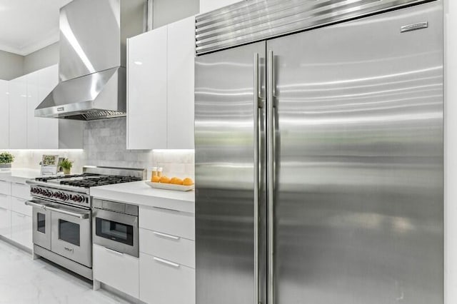 kitchen with high quality appliances, white cabinets, backsplash, and wall chimney exhaust hood