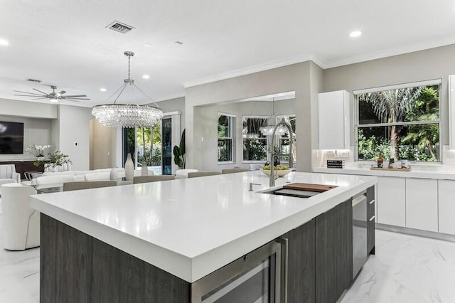 kitchen with sink, a kitchen island with sink, dark brown cabinetry, white cabinets, and ceiling fan with notable chandelier