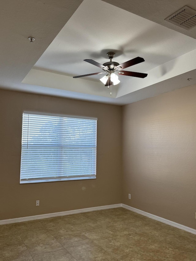 unfurnished room with a tray ceiling, plenty of natural light, and ceiling fan