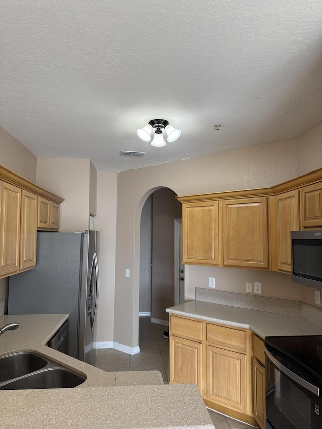 kitchen featuring sink, light tile patterned flooring, a textured ceiling, and appliances with stainless steel finishes