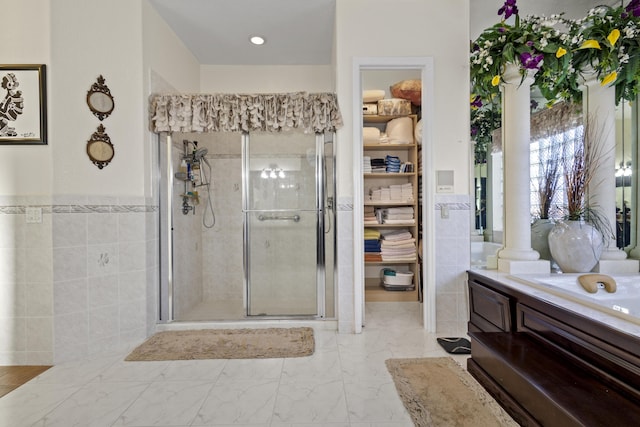 bathroom with vanity, walk in shower, tile walls, and decorative columns