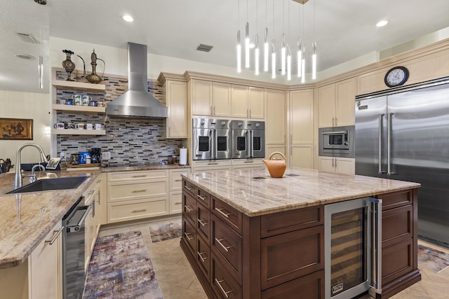 kitchen with built in appliances, beverage cooler, wall chimney range hood, and light stone counters