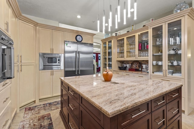 kitchen with decorative light fixtures, light stone counters, built in appliances, and dark brown cabinets