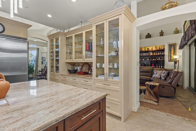 kitchen featuring cream cabinets, light tile patterned flooring, stainless steel built in refrigerator, and light stone countertops