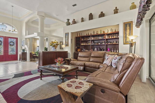 living room with decorative columns, french doors, a raised ceiling, light tile patterned flooring, and a high ceiling