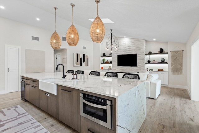 kitchen with sink, hanging light fixtures, vaulted ceiling, light stone countertops, and an island with sink