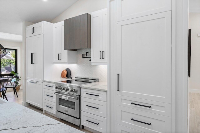 kitchen with wall chimney exhaust hood, white cabinetry, stainless steel stove, and vaulted ceiling