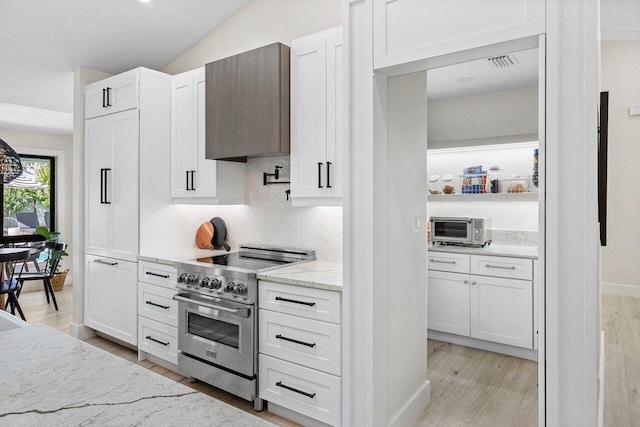 kitchen with white cabinets, light stone counters, wall chimney range hood, and stainless steel stove