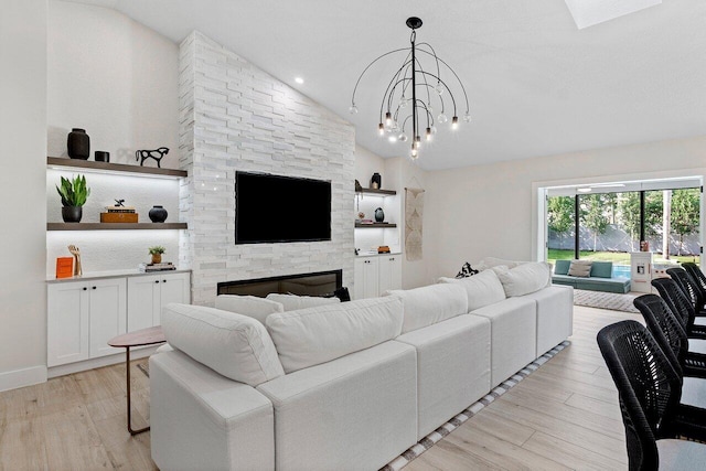 living room featuring a chandelier, light wood-type flooring, vaulted ceiling, and a stone fireplace