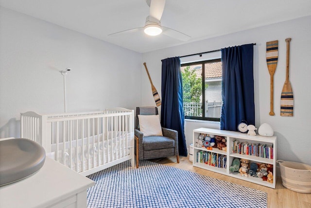 bedroom featuring ceiling fan, wood-type flooring, and a nursery area