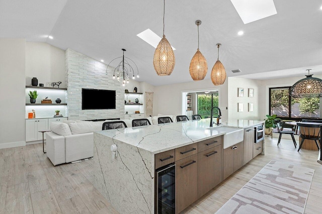 kitchen featuring sink, an inviting chandelier, wine cooler, a spacious island, and vaulted ceiling with skylight