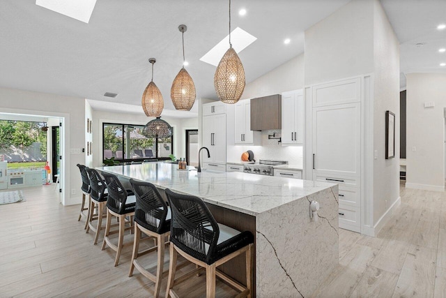 kitchen with light stone counters, sink, decorative light fixtures, white cabinets, and a large island