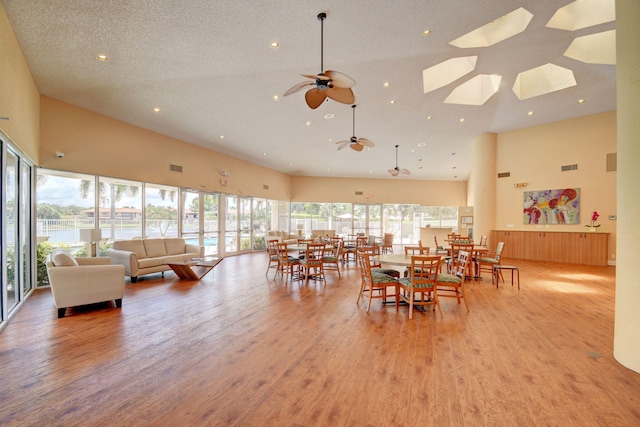 dining room with ceiling fan, a healthy amount of sunlight, a towering ceiling, and light hardwood / wood-style flooring